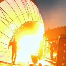 Silhouette of people by a hot air balloon being inflated, with a warm glow against a dusk sky.