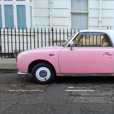 A classic style Nissan Figaro in pastel pink parked on a London street.