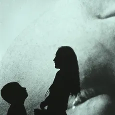 Silhouettes of two people in profile facing each other, set against a textured grayscale background. One figure appears shorter, looking up, while the taller figure looks down.