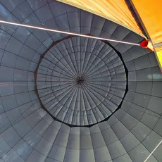 Interior view of a hot air balloon's vent, showcasing the geometric patterns and bright orange fabric.