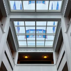 View of the Stadsarchief Amsterdam interior, featuring a grid skylight with geometric designs on white walls. The ceiling showcases colorful windows and lit ceiling lamps, creating an open and bright atmosphere.