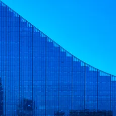 Curved glass building under evening sky with visible crescent moon. Reflections and silhouettes add detail to the modern architectural design.