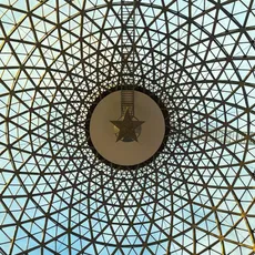 View of a glass dome with a geometric grid pattern at Panora mall in Ankara. The structure forms a symmetrical design with a large circular element and a star in the center, allowing natural light to filter through.