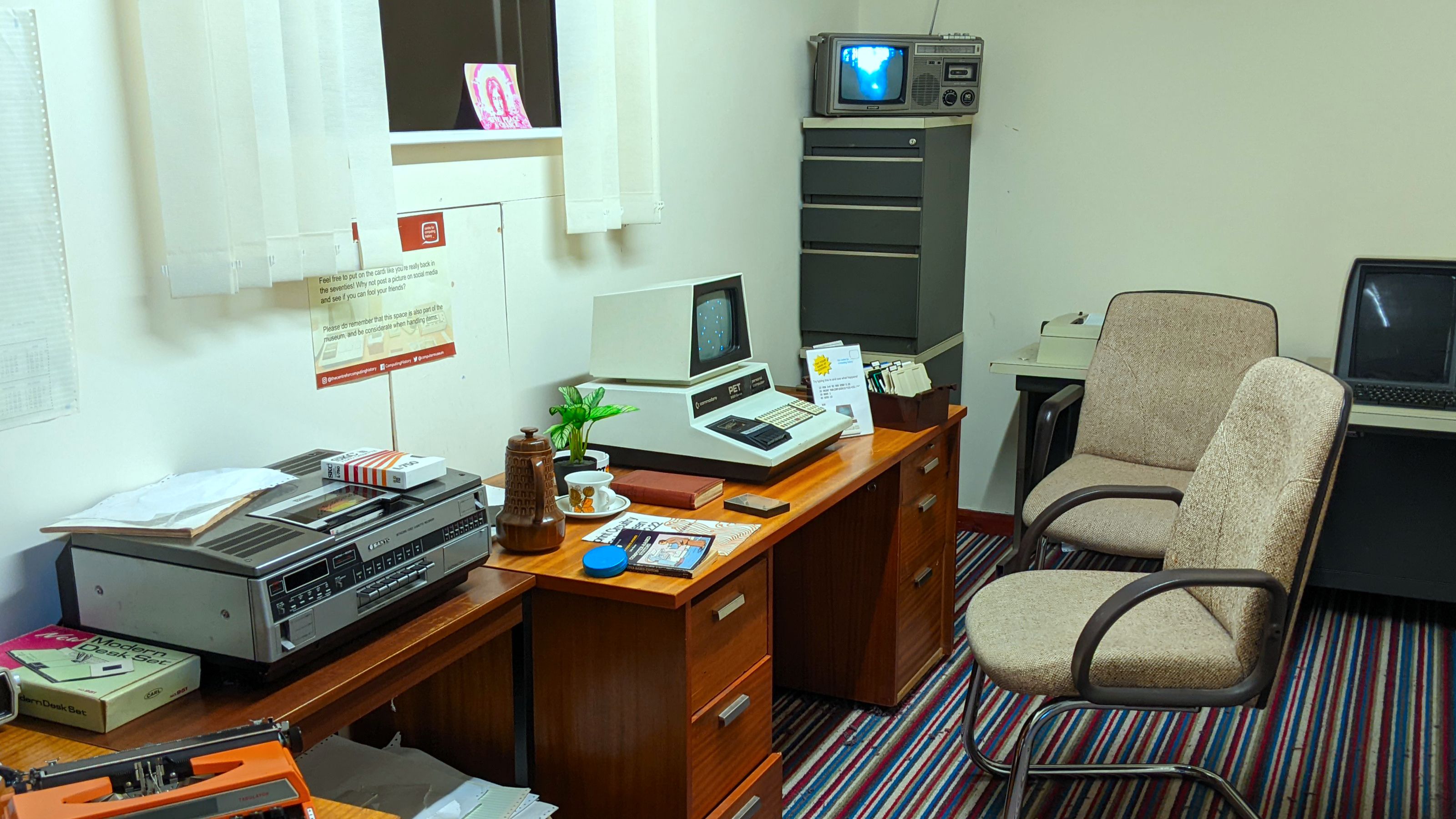 Vintage 1970s office setup with a retro computer, typewriter, old television, and office chairs.