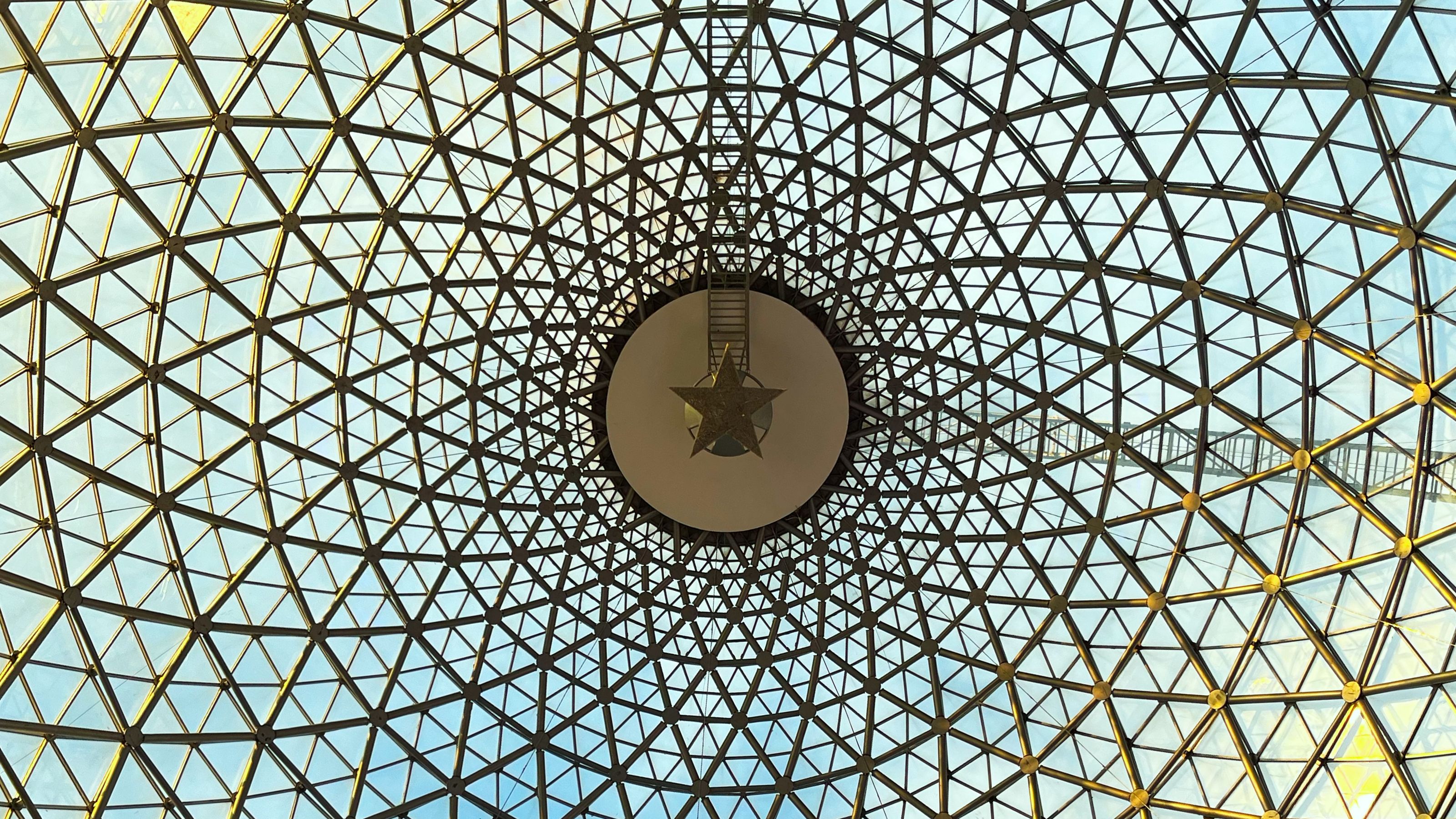 View of a glass dome with a geometric grid pattern at Panora mall in Ankara. The structure forms a symmetrical design with a large circular element and a star in the center, allowing natural light to filter through.